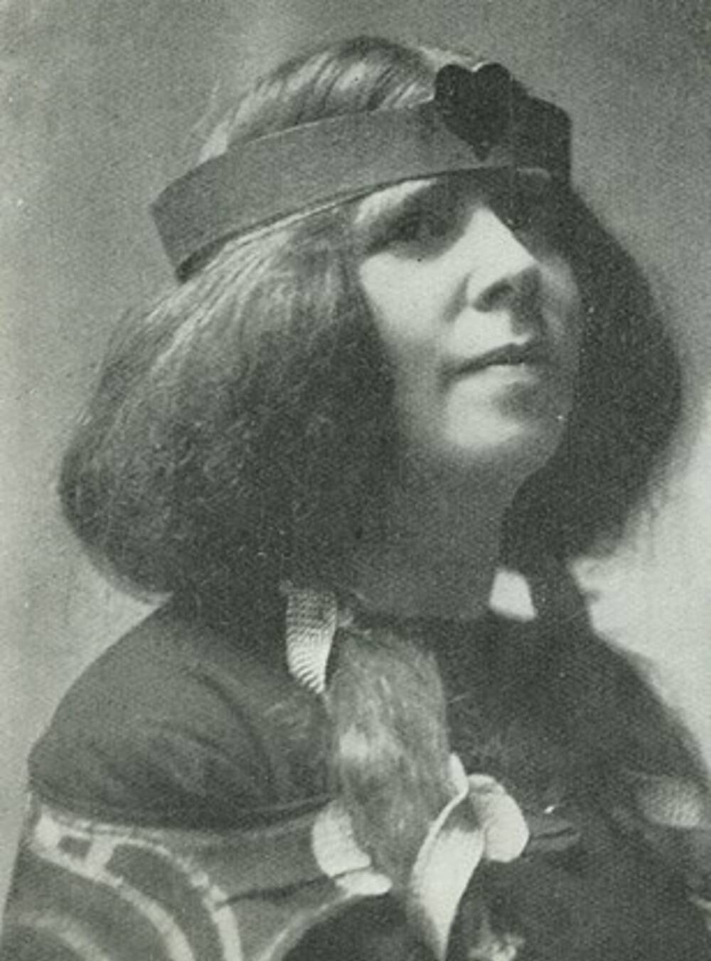A black and white photograph of a young woman. She wears a headband with a heart at the front over her long voluminous hair. She also appears to be wearing a shawl over her dark top.