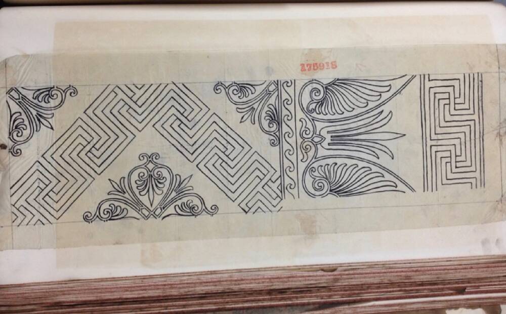 A black and white line drawing of a carpet design is taped into an old large book. The design includes an Escher-esque path border, surrounding stylised floral motifs.