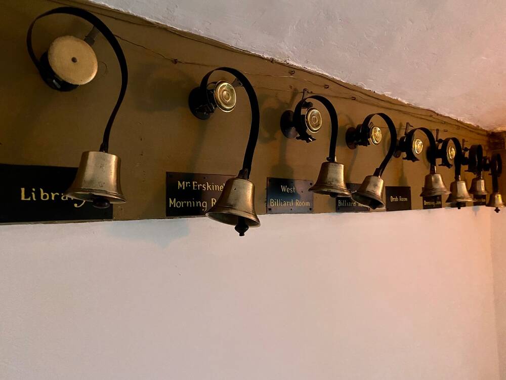 A row of old-fashioned servants' bells mounted to a wall, with the name of a room underneath each one.