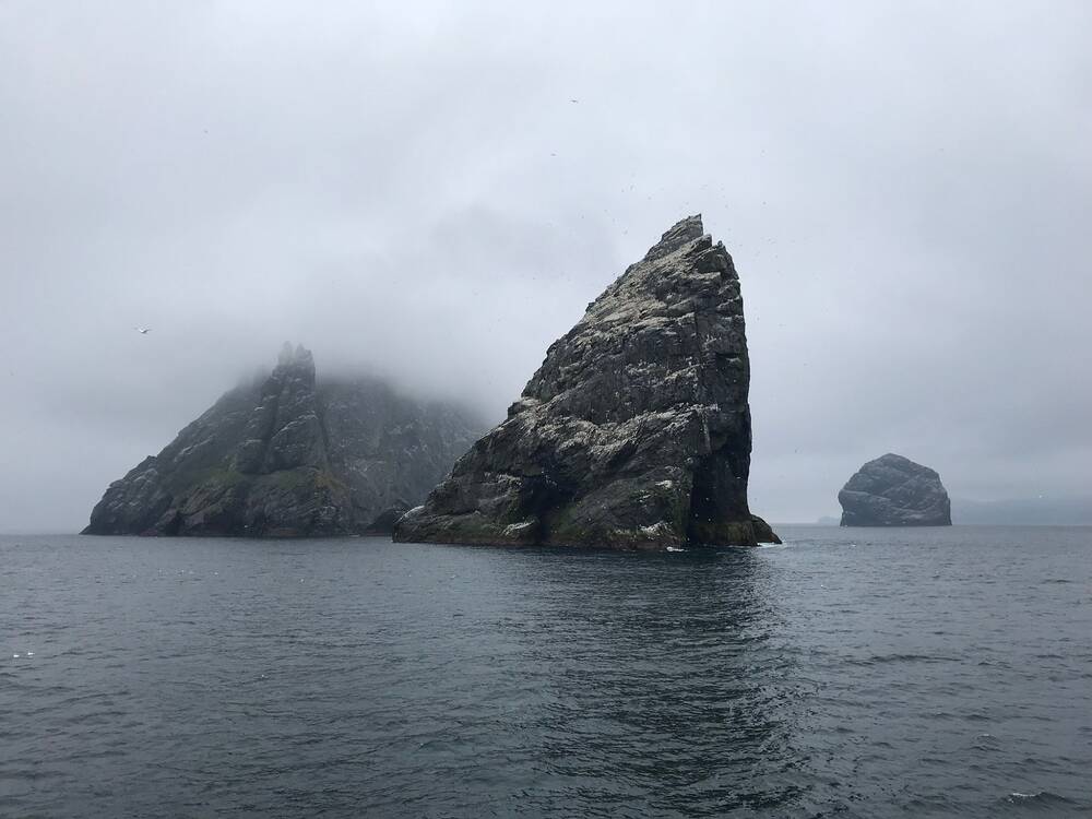 Large sea stacks tower out of the sea, with their tops capped by swirling mist.