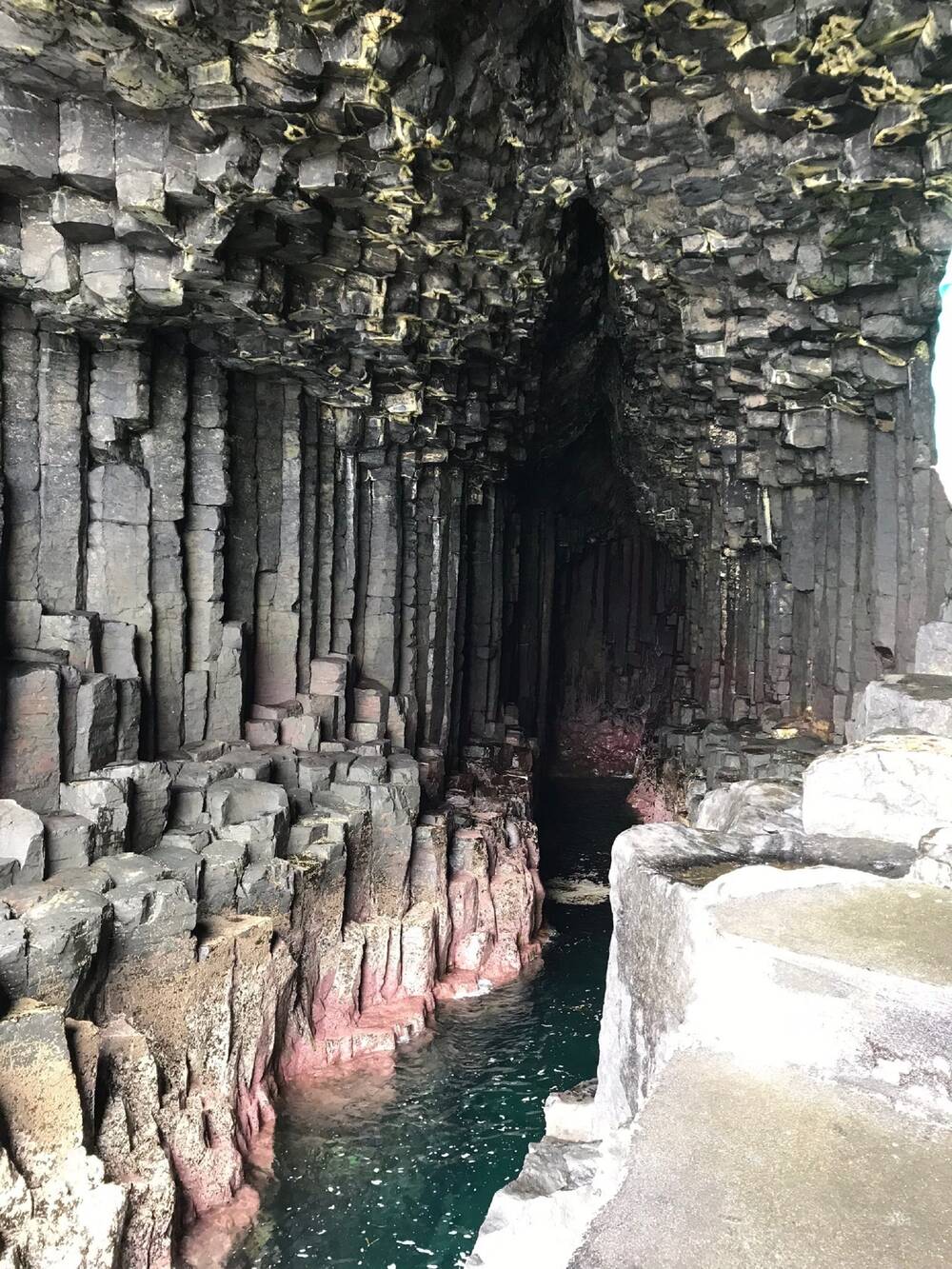 A view looking into a cave, with turquoise water at the bottom. The walls are made up of columns of rock, rather like row upon row of Kit-Kats!
