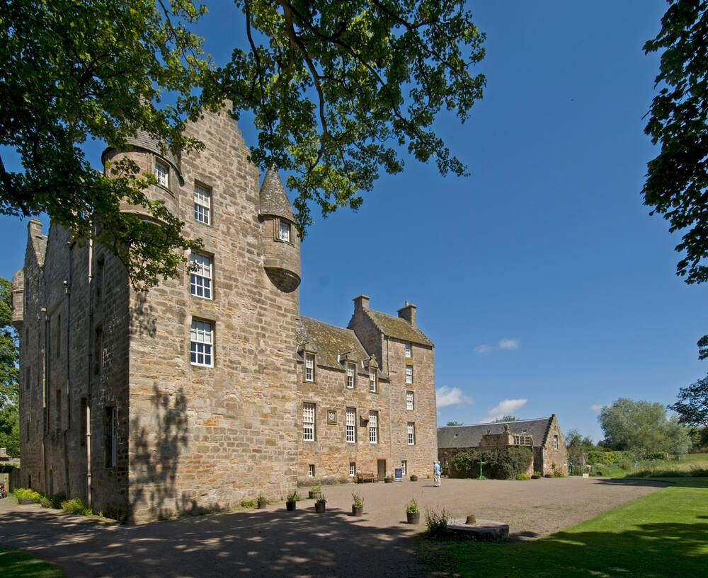 A view of Kellie Castle on a sunny day with bright blue sky behind. A tall corner tower with turrets is closest to the camera. A large tree frames the shot.