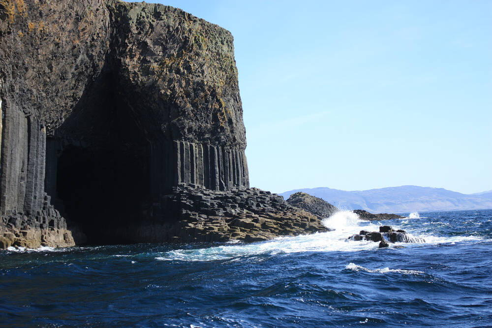 Fingal's Cave on Staffa, seen from the sea. White breakers crash against the rock beside the cave entrance. The basalt columns can also be seen either side of the entrance.