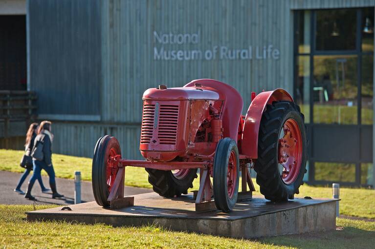 A red tractor stands on a display board in front of the National Museum of Rural Life