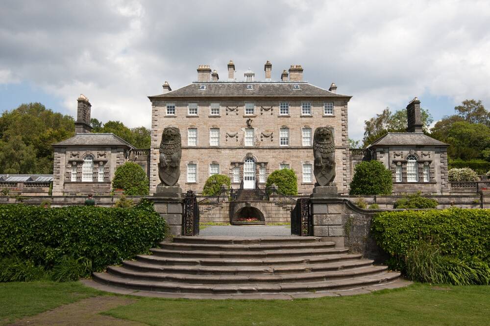 A view of the back of Pollok House on a bright day, with wide stone steps leading up to the parterre gardens directly outside the house. The house is a classic Georgian 'square' shape, with a small wing either side.