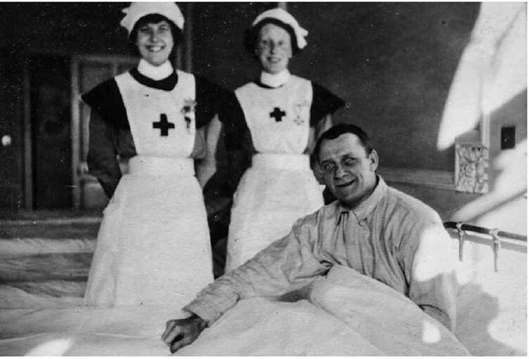A black and white photograph of two smiling nurses, standing beside a smiling patient in bed.