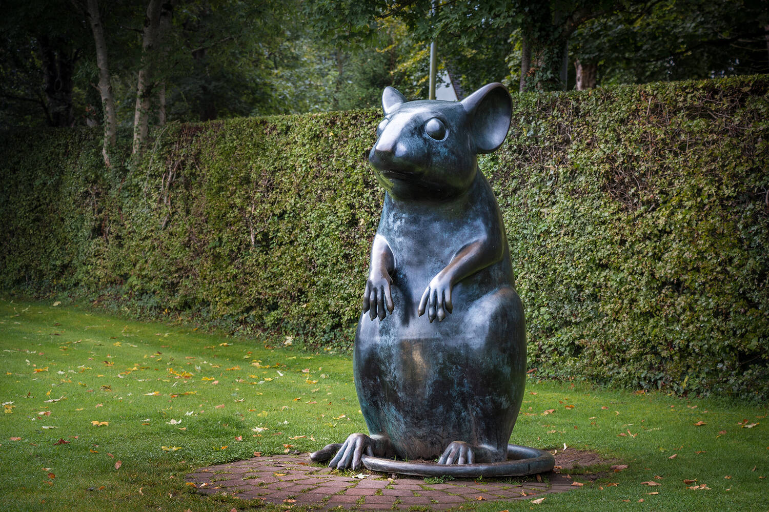 A large statue of a mouse sitting up on its hind legs with its tail wrapped around the base.