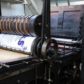A close-up view of the Wharfedale reliance printing press, showing a large poster rolled around a wheel.