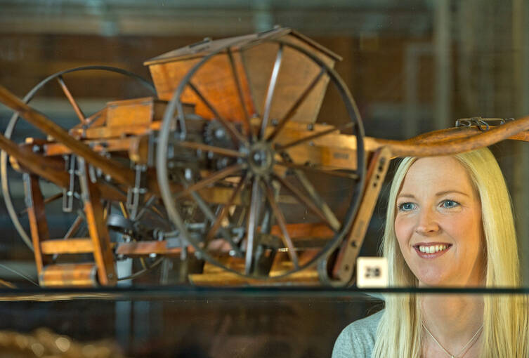 A young woman looks at a model of an old ploughing cart in a museum.