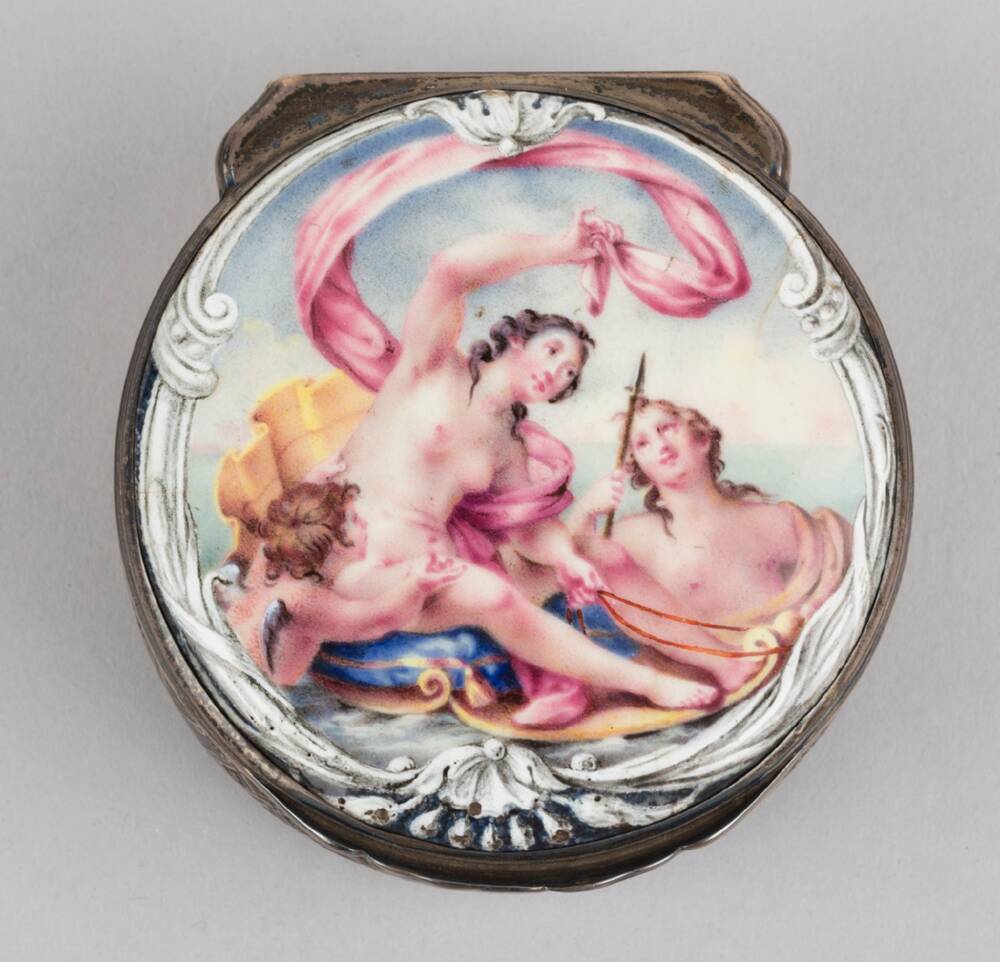 A small pill box with a ceramic hinged lid (closed) is displayed against a plain grey background. The picture on the box is of a classical woman riding on a shell, surrounded by two other classical figures.