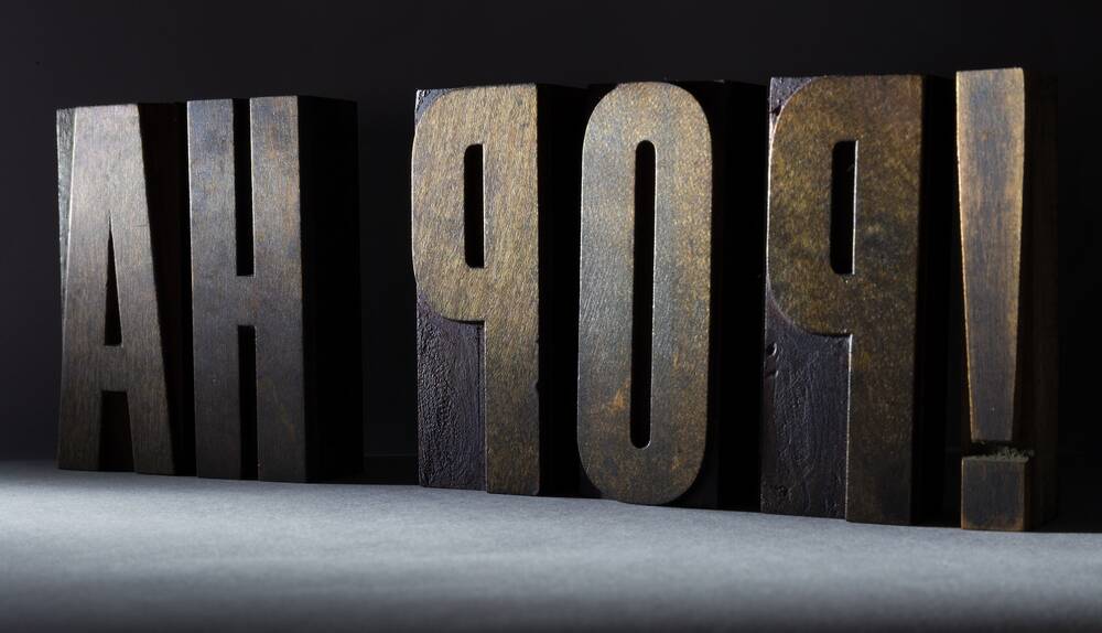 Pieces of wooden type stand in a row, showing a mirror image of the phrase Ah pop!