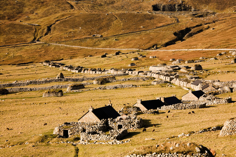 A line of small stone cottages in a barren landscape. There is a head dyke behind them.