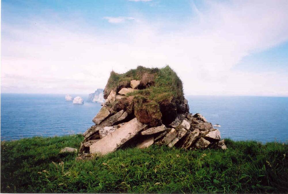 A small cleit stands on the top of a hill on St Kilda, with the sea and the island of Boreray visible in the distance. From the outside, it rather resembles a pile of stones with turf on top.
