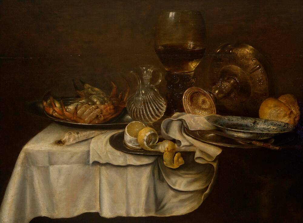 A still life oil painting of a table piled with rich food upon a white cloth. At the right is an upended crab on a silver platter. Beside it stand a water jug and an enormous goblet. On the right, another large goblet lies on its side.