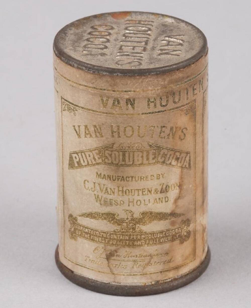 An old tin of hot chocolate, with ‘Van Houten’s Cocoa’ embossed in the metal at the top, and a browning and faded label wrapped all around the body of the tin.