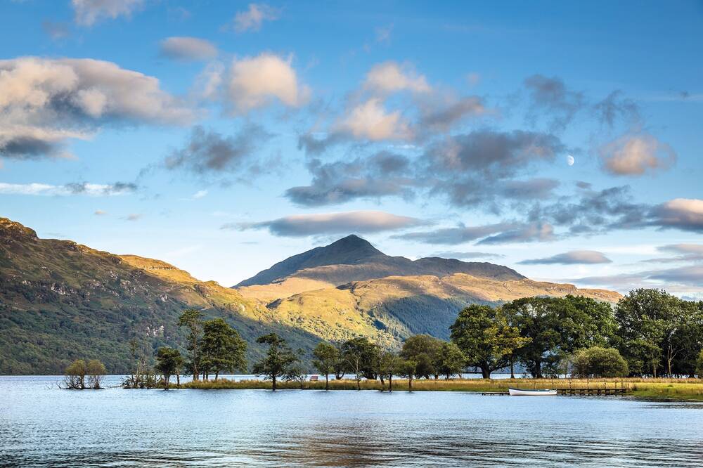 A view of a tall mountain with a pointed summit, seen from across a loch on a sunny day.