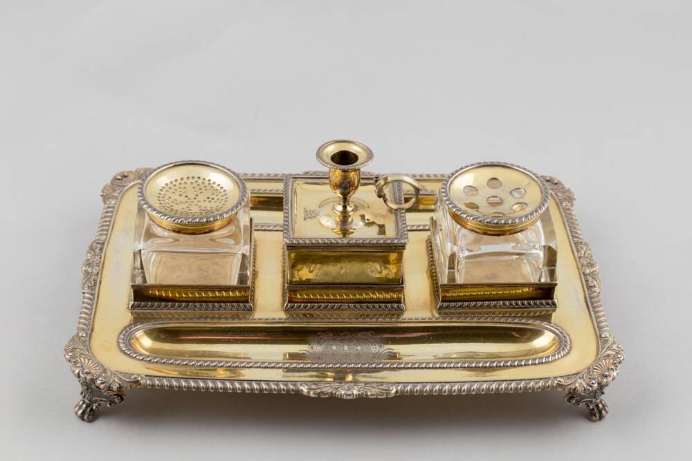 A silver writing set that includes a silver and gilt oblong inkstand, ink pot and pounce pot.