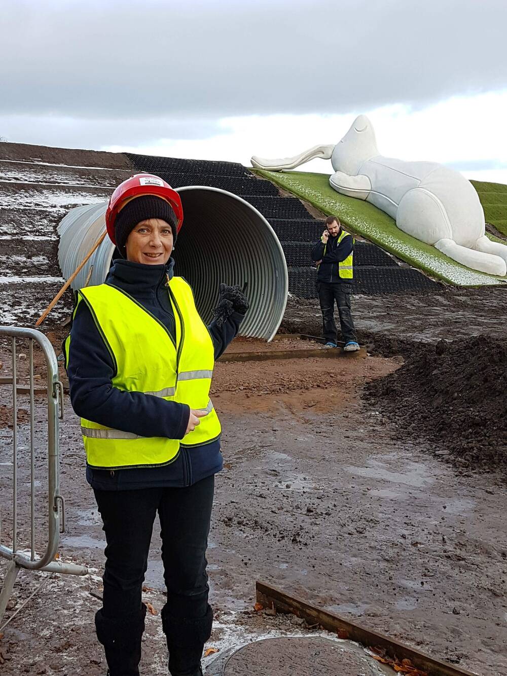 A woman in a hard hat and hi-vis jacket is standing in the Playful Garden at Brodie Castle when it was under construction. The large white sculpture of Brodie Bunny is in the background.