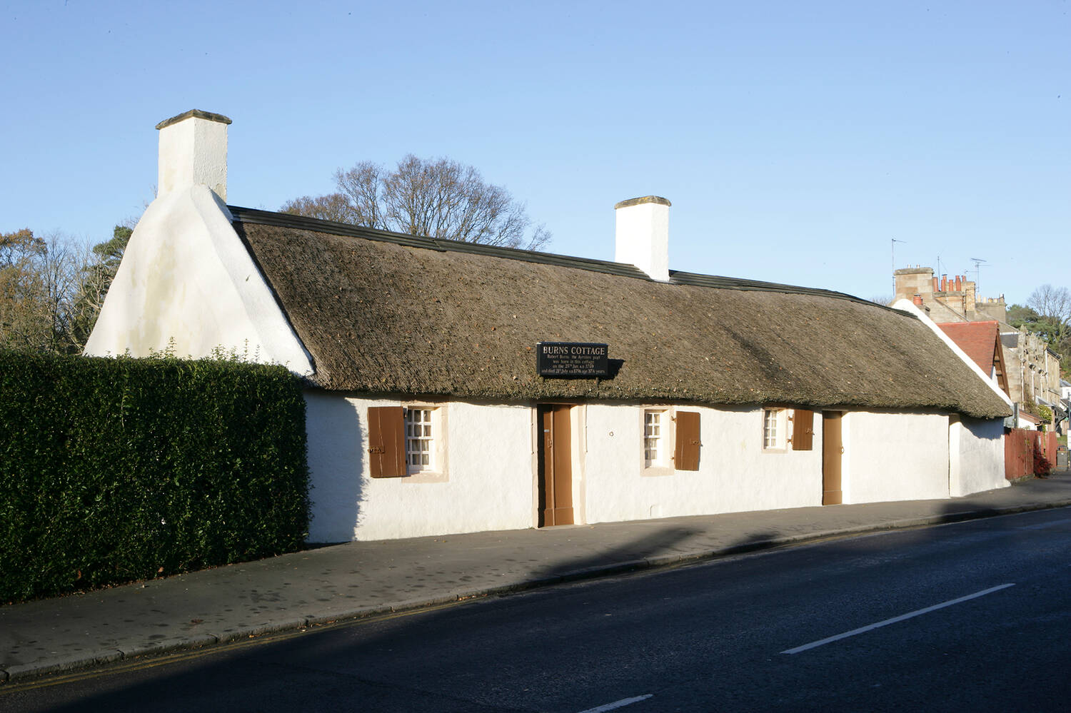 A white thatched cottage stands on the side of a road with a blue sky background.