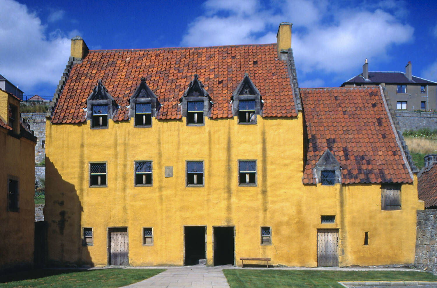 The front of ochre-coloured Culross Palace on a bright sunny day, blue sky visible above the tiled roof.