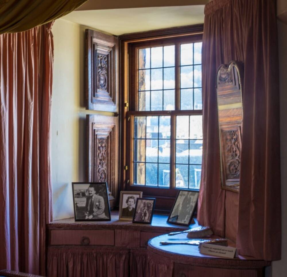 A boudoir decorated in pale pink silk, looking towards a window which has several framed black and white photographs of people.