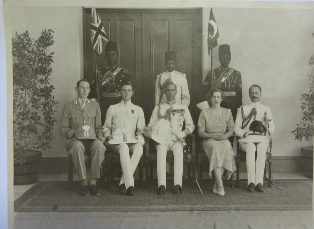 Black and white group photograph showing a colonial governor general in uniform. A woman sits to his left and three other men are on the front row. Three men of colour stand behind them.