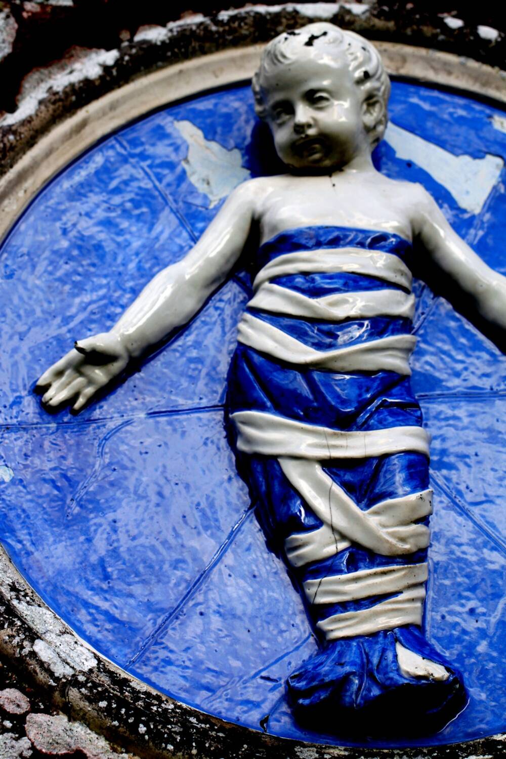 Close-up of a circular terracotta ware plaque, painted blue, showing a swaddled child.