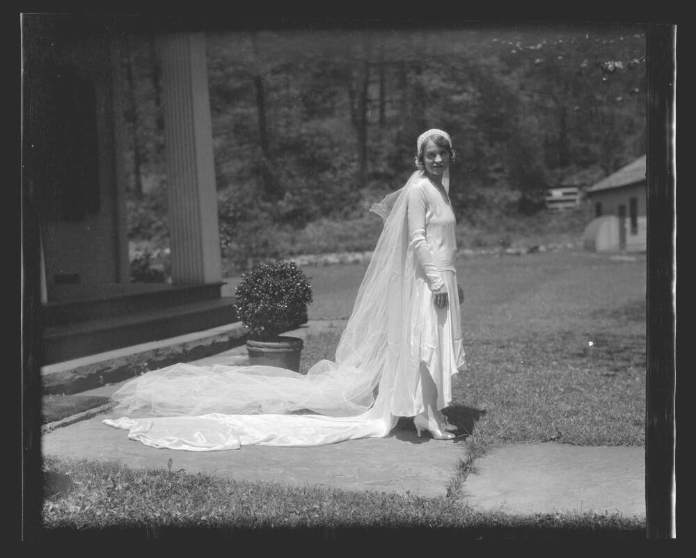 Black and white photograph of a woman in a 1920s style wedding dress with a long train and veil.