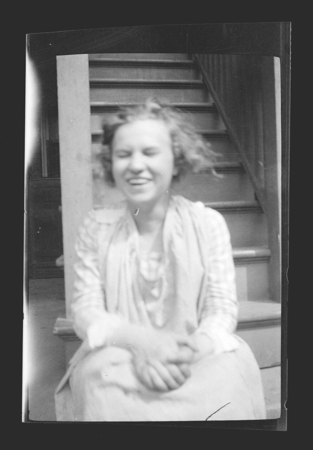 Black and white photograph of a young woman, sitting at the bottom of a staircase and laughing.