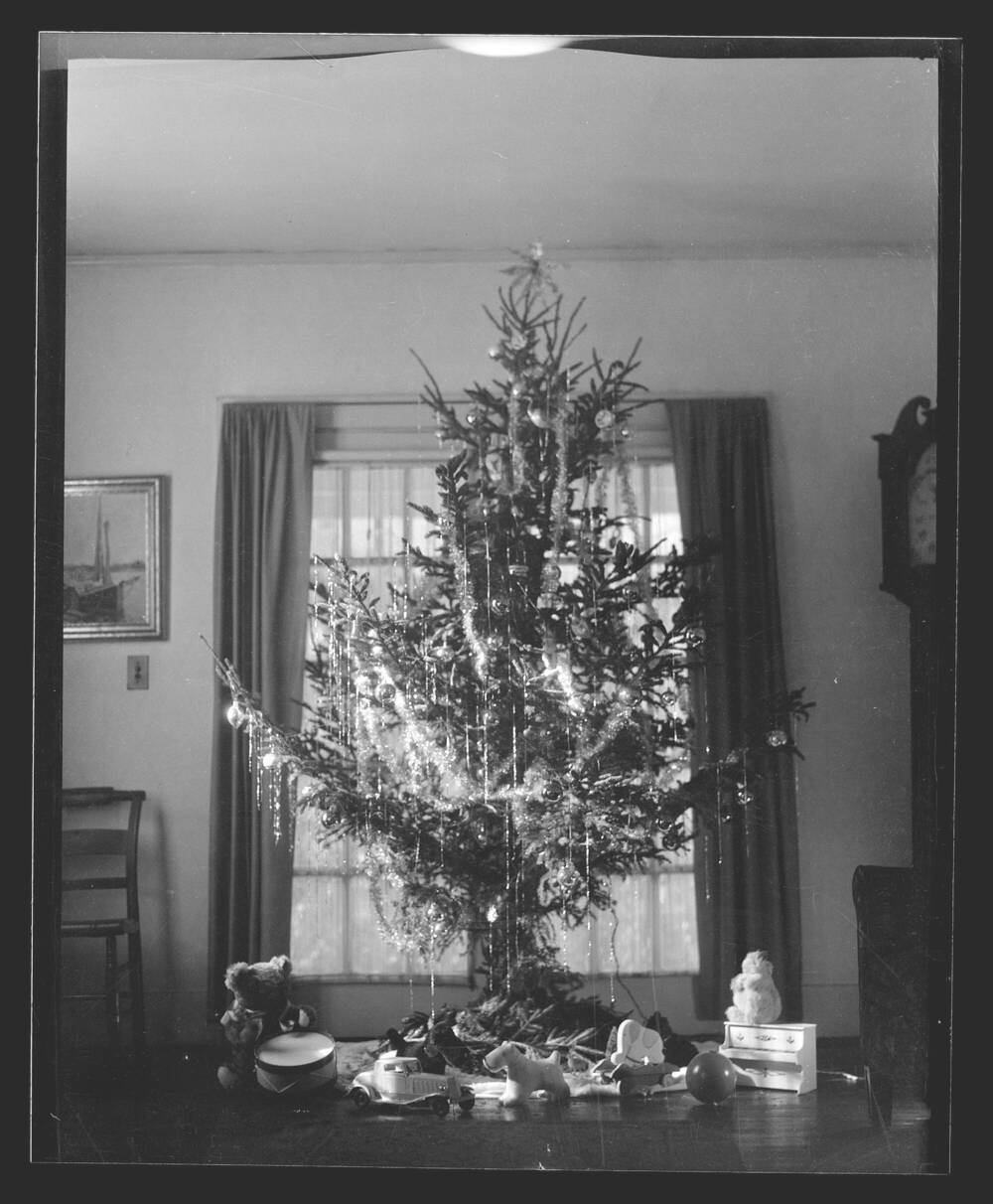 Black and white photograph of a Christmas tree on a table, decorated with tinsel and lights.
