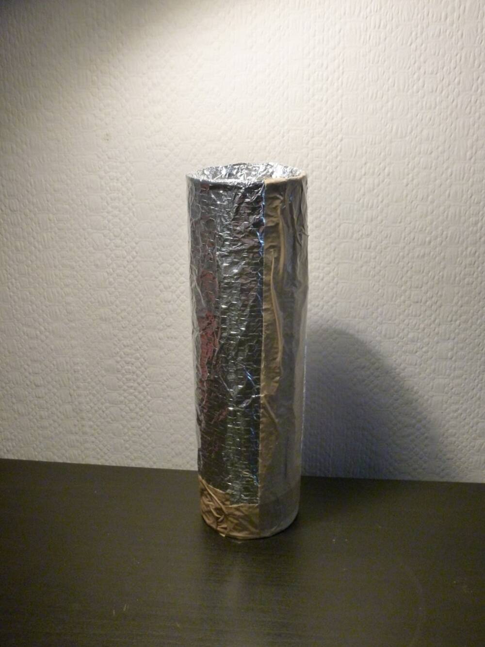 A Pringles tube wrapped in foil, on a black table.