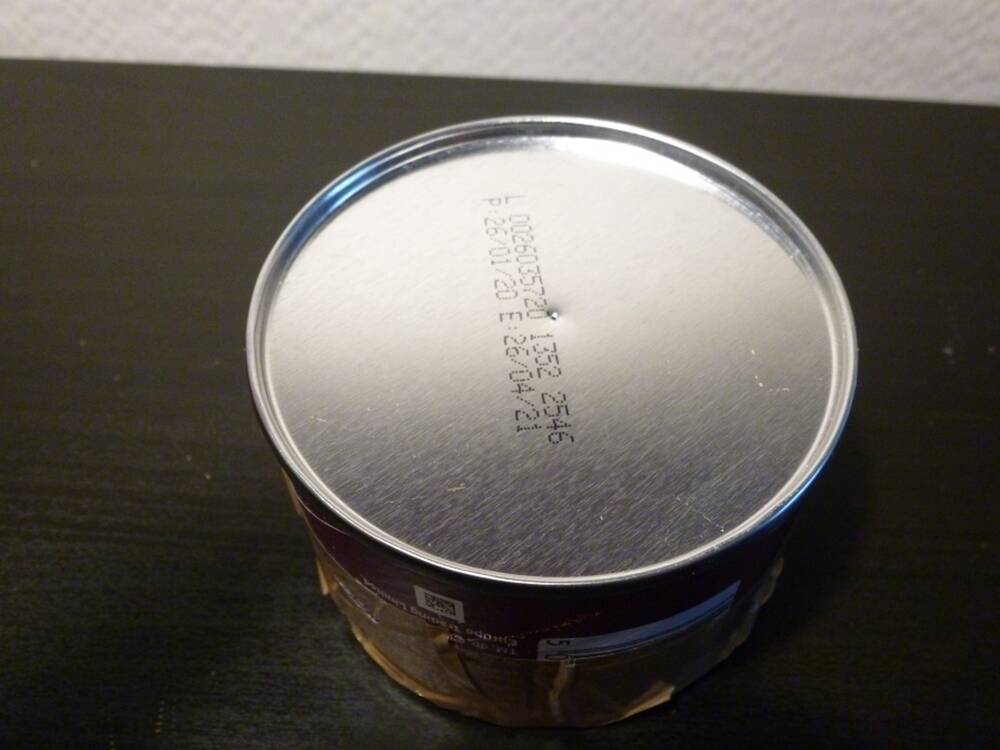 The metal bottom of a Pringles tube with a pin hole in the centre, on a black table.