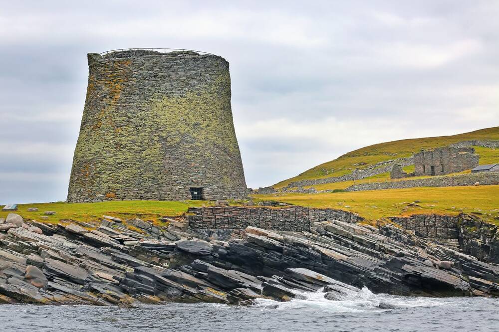 A large stone broch in a barren, rocky landscape by the sea.
