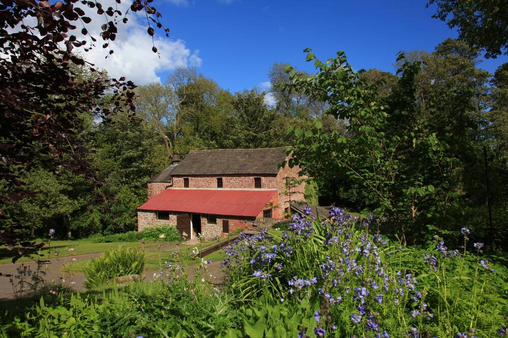 A mill is set in lush countryside under a blue sky.